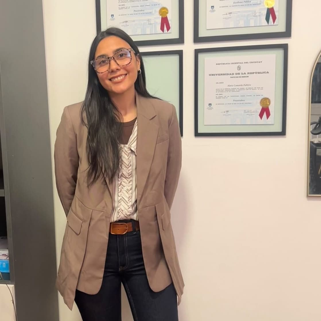 Giuliana Mercadante de pie frente a diplomas enmarcados.